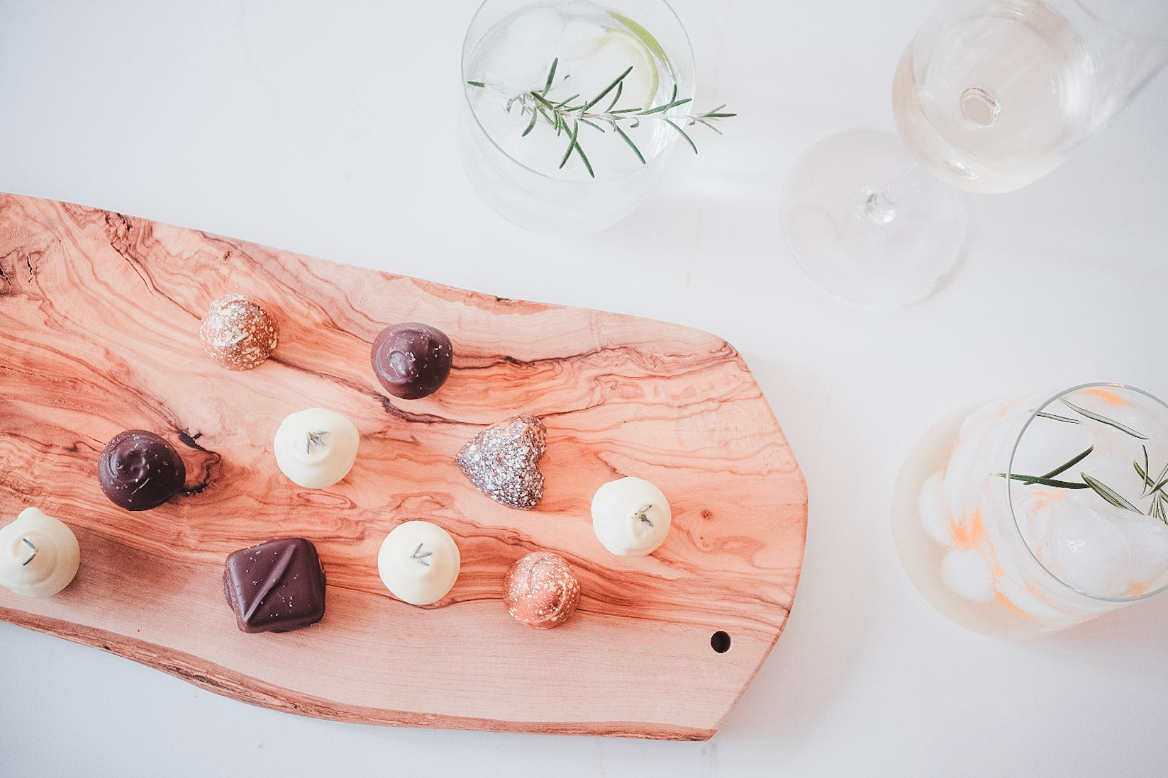 Wooden cutting board with various small desserts on a white surface