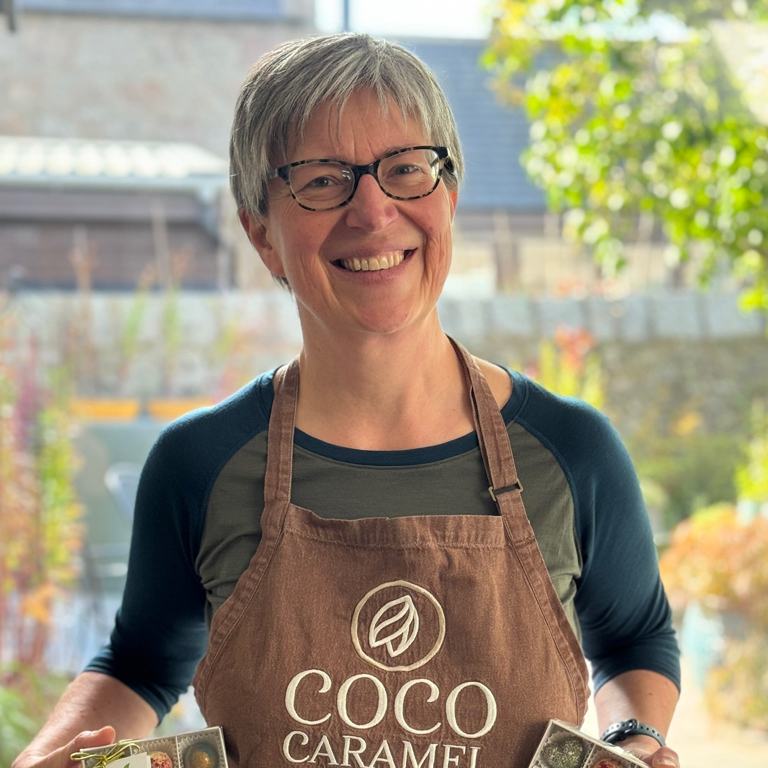 Person wearing a 'Coco Caramel' apron holding chocolate boxes outdoors.